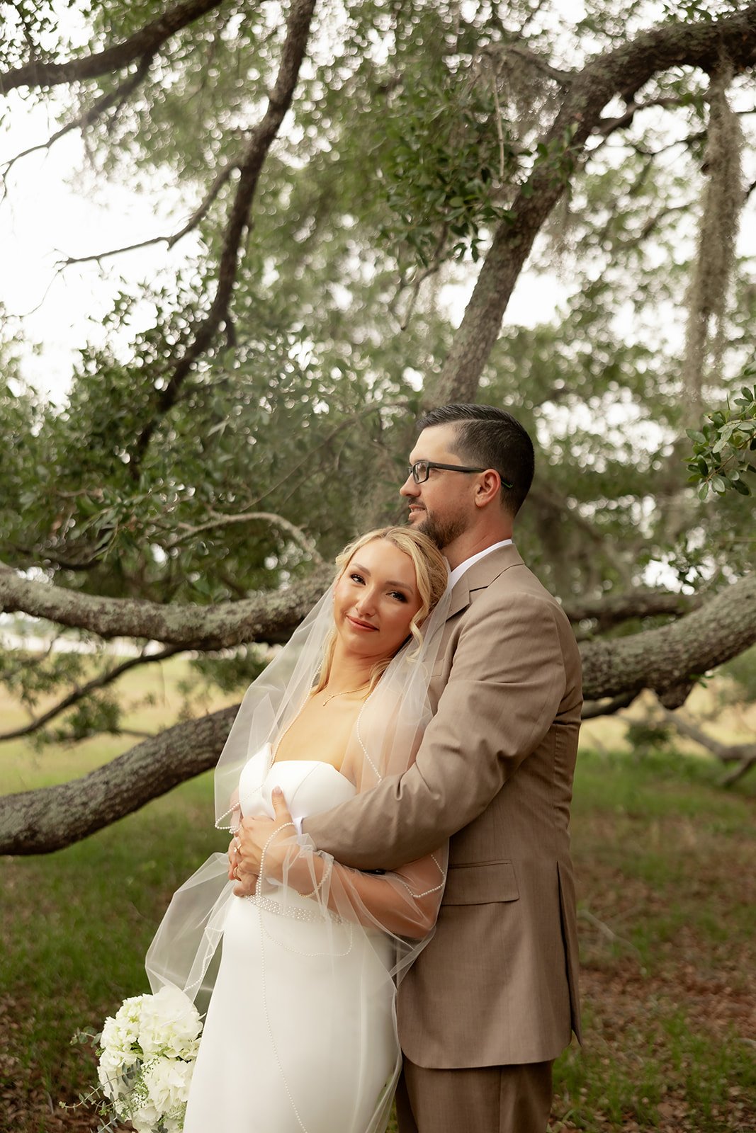 Bride and groom embracing under live oak tree at Browns Grove Sarasota, bride looking at camera