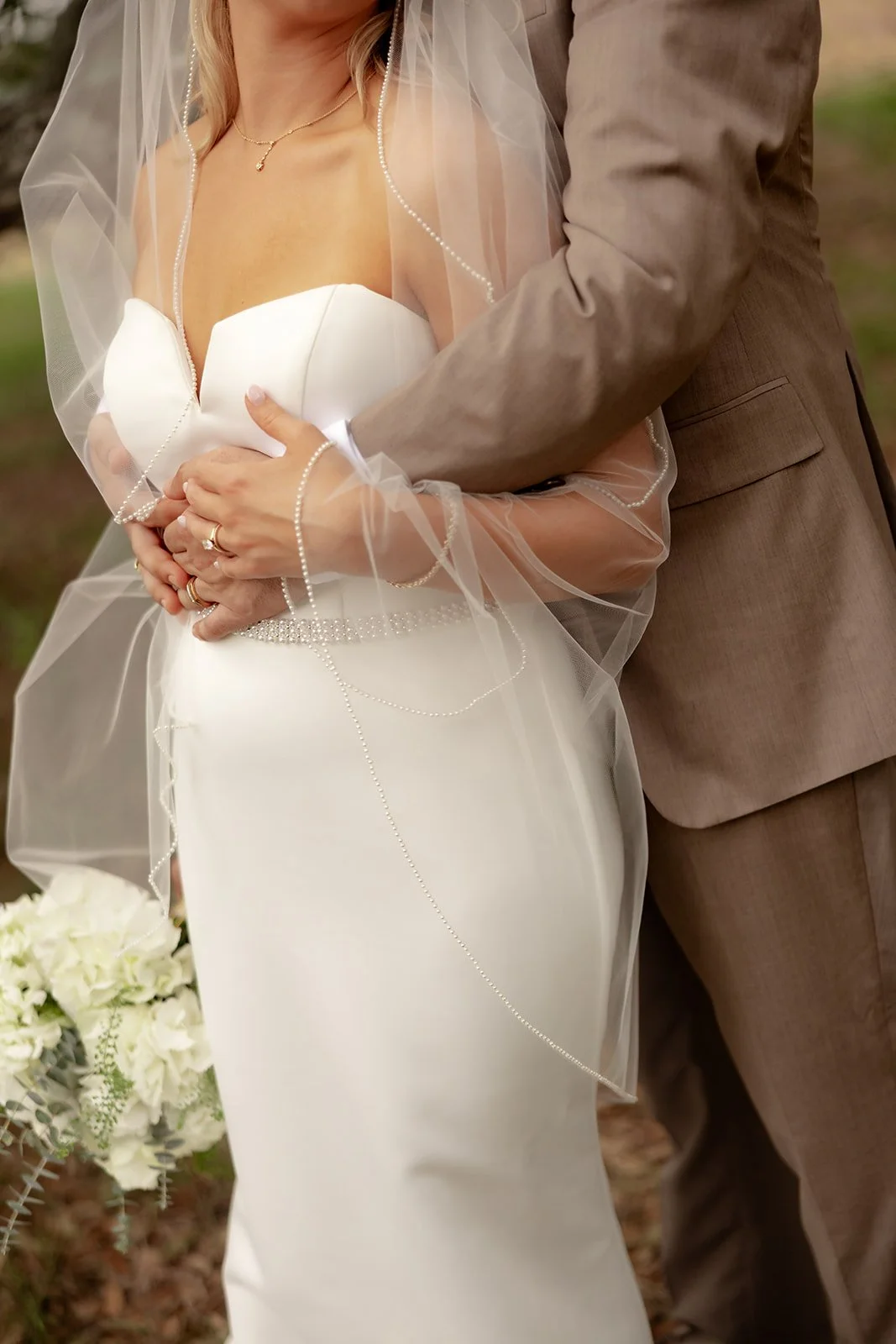 Detail of bride and groom's clasped hands showing wedding rings with pearl-edged veil at Browns Grove Sarasota