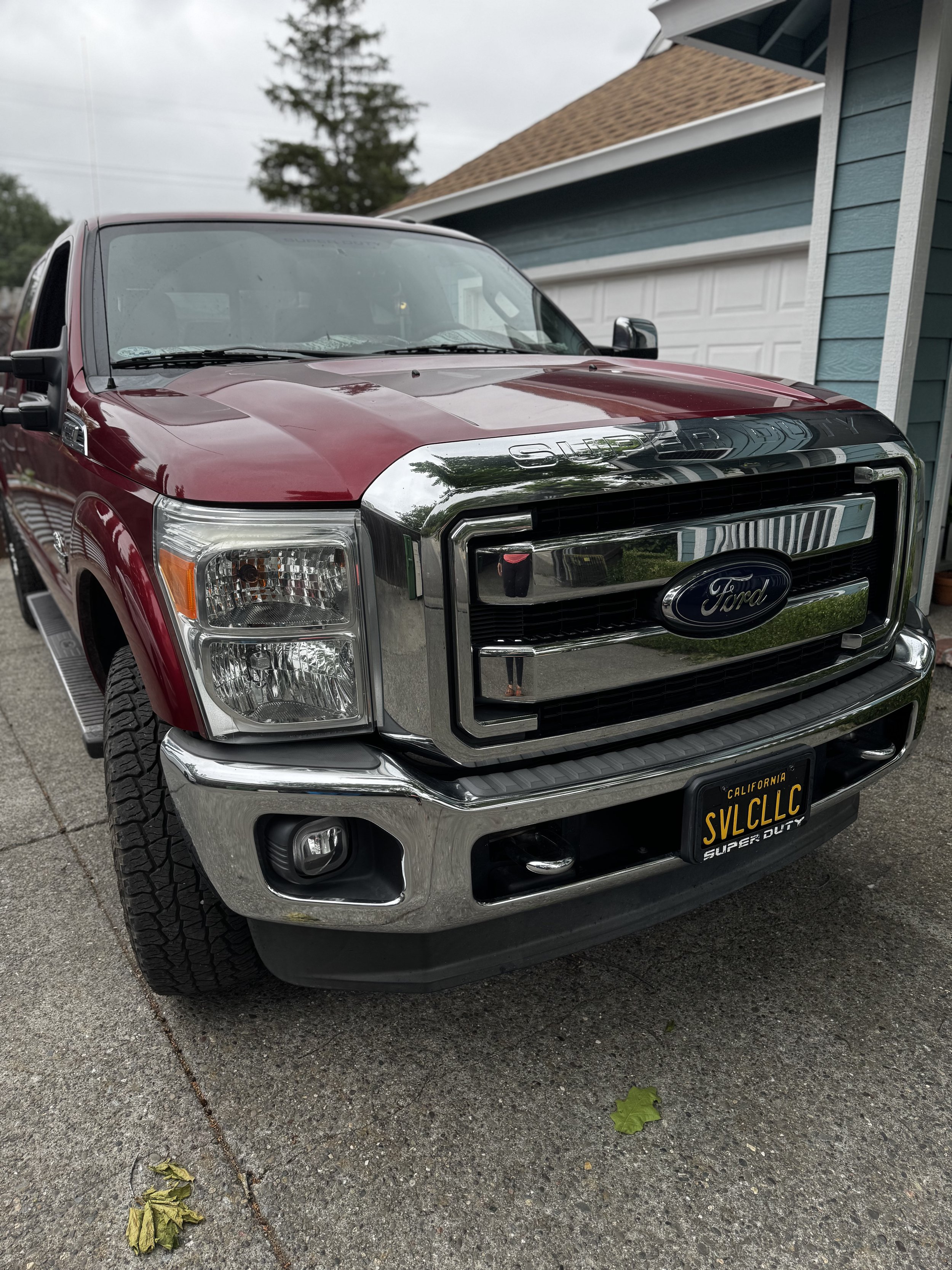 Red Ford Super Duty truck parked in a driveway next to a blue house.