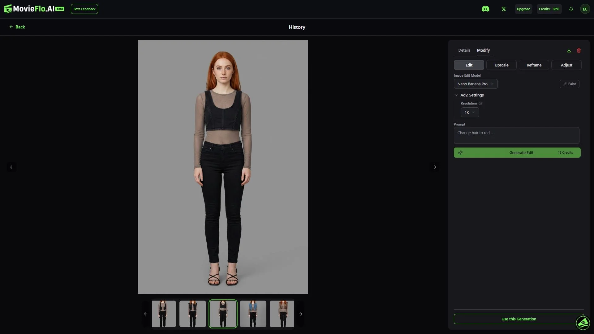 A young woman with long red hair wearing a black crop top with sheer long sleeves and high-waisted black pants, standing against a plain gray background.
