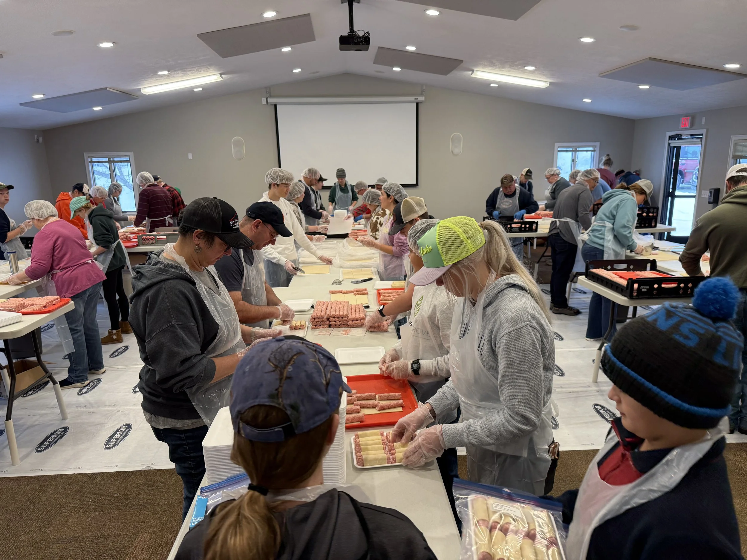 People wearing hairnets and aprons working together at a long table preparing Pigs in a Blanket