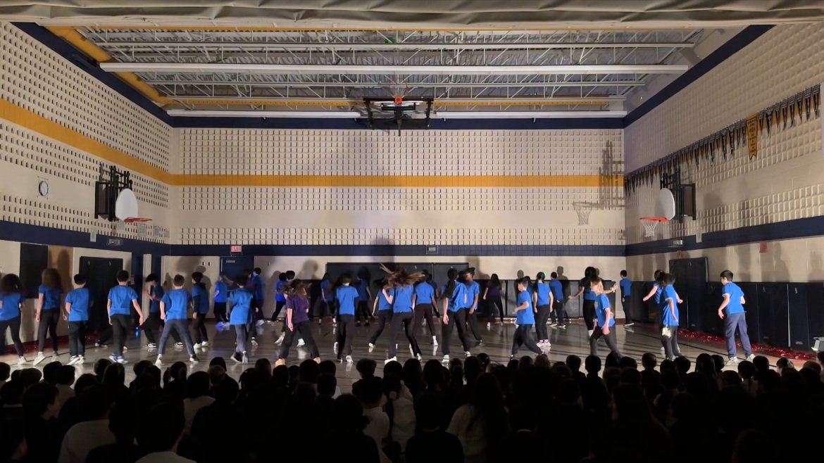 A group of people wearing blue shirts performing in a gymnasium with an audience watching.