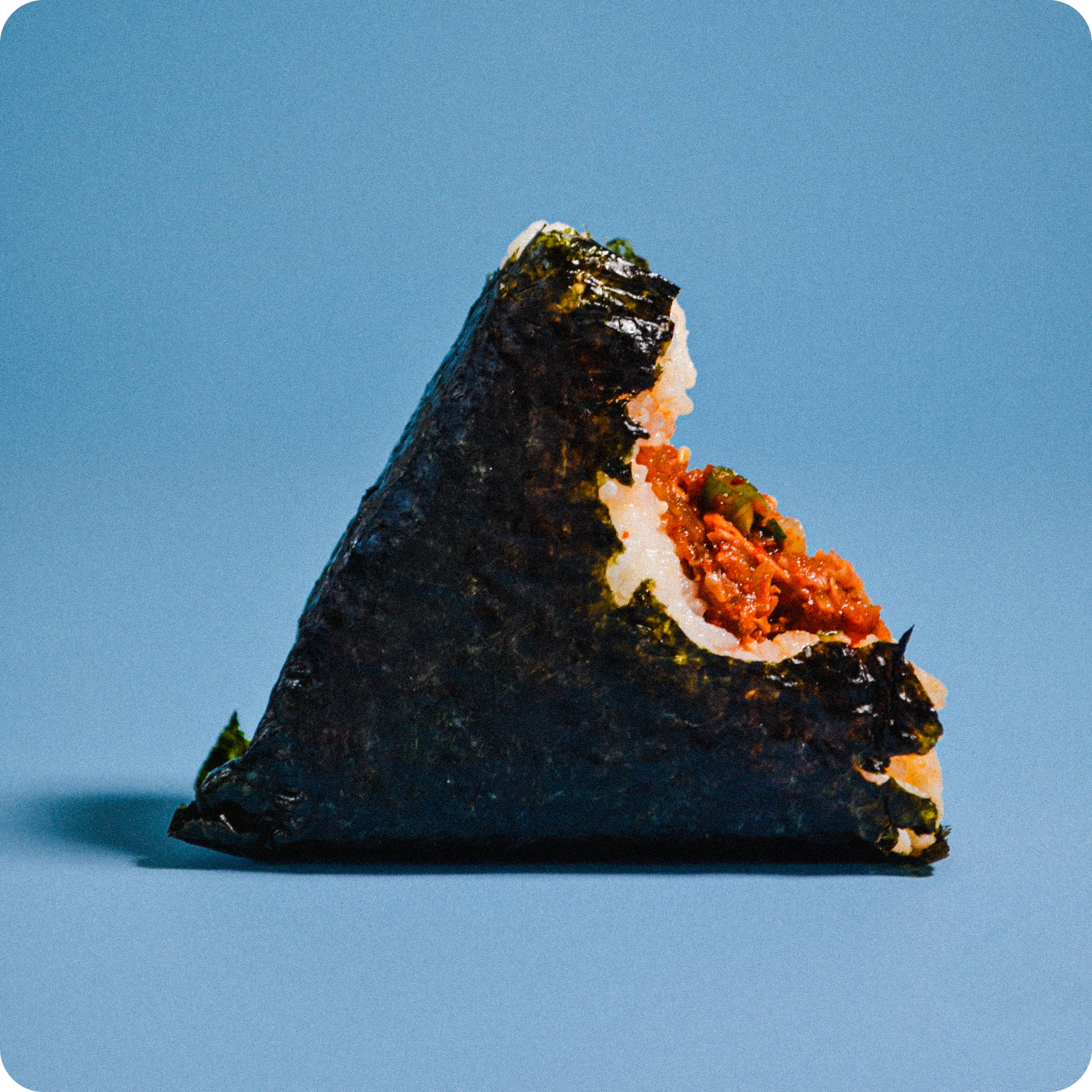 Close-up of an unwrapped Go-bop snack with seaweed wrapping, rice, and delicious filling inside, set against a blue background.