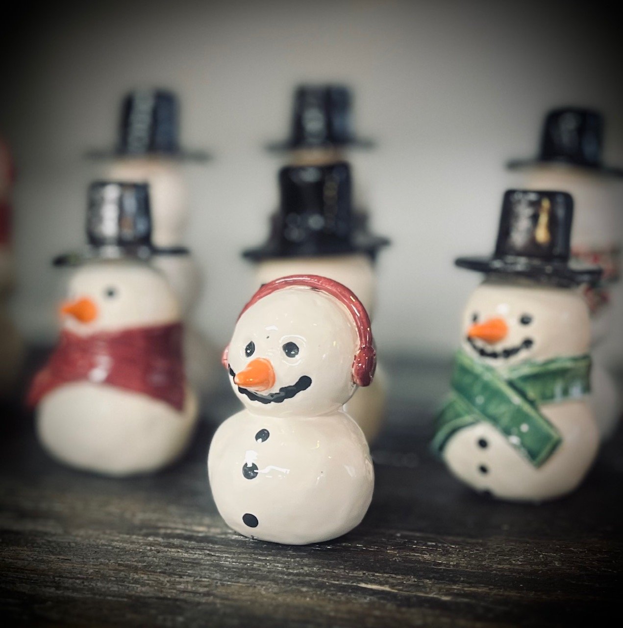 Decorative snowman figurines wearing different accessories, with a focus on the snowman in the foreground with a red hat and headphones, set on a wooden surface.
