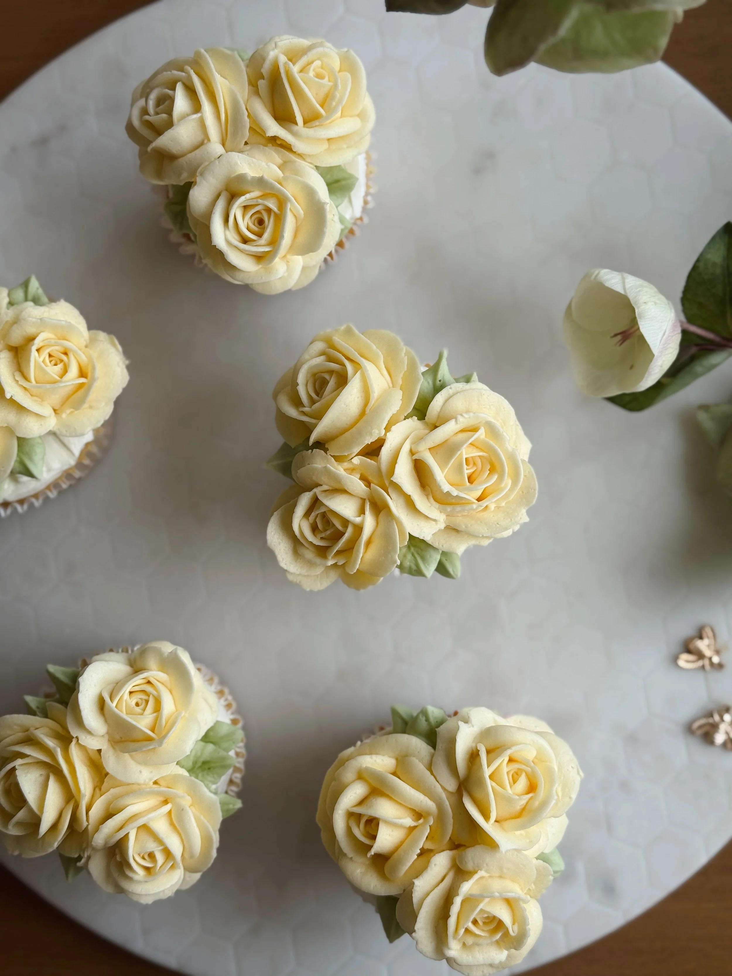 Cupcakes decorados con glaseado en forma de rosas de color crema, colocados sobre una bandeja blanca de superficie hexagonal.