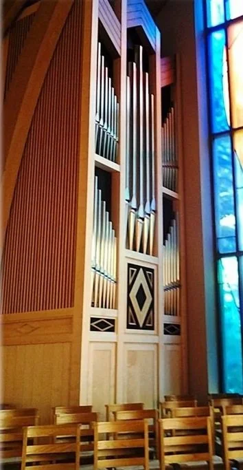 Large pipe organ with wooden panels and stained glass windows in the background.