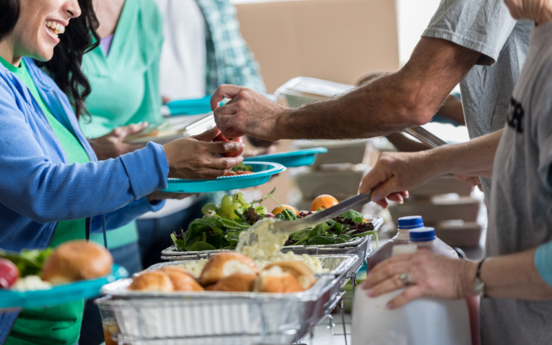 People serving themselves food at a buffet with salads, bread rolls, and drinks.
