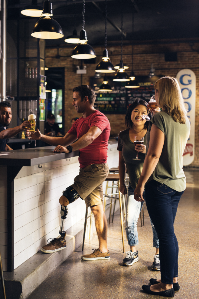People at a bar, including a man with a prosthetic leg, engaging in conversation and drinks.