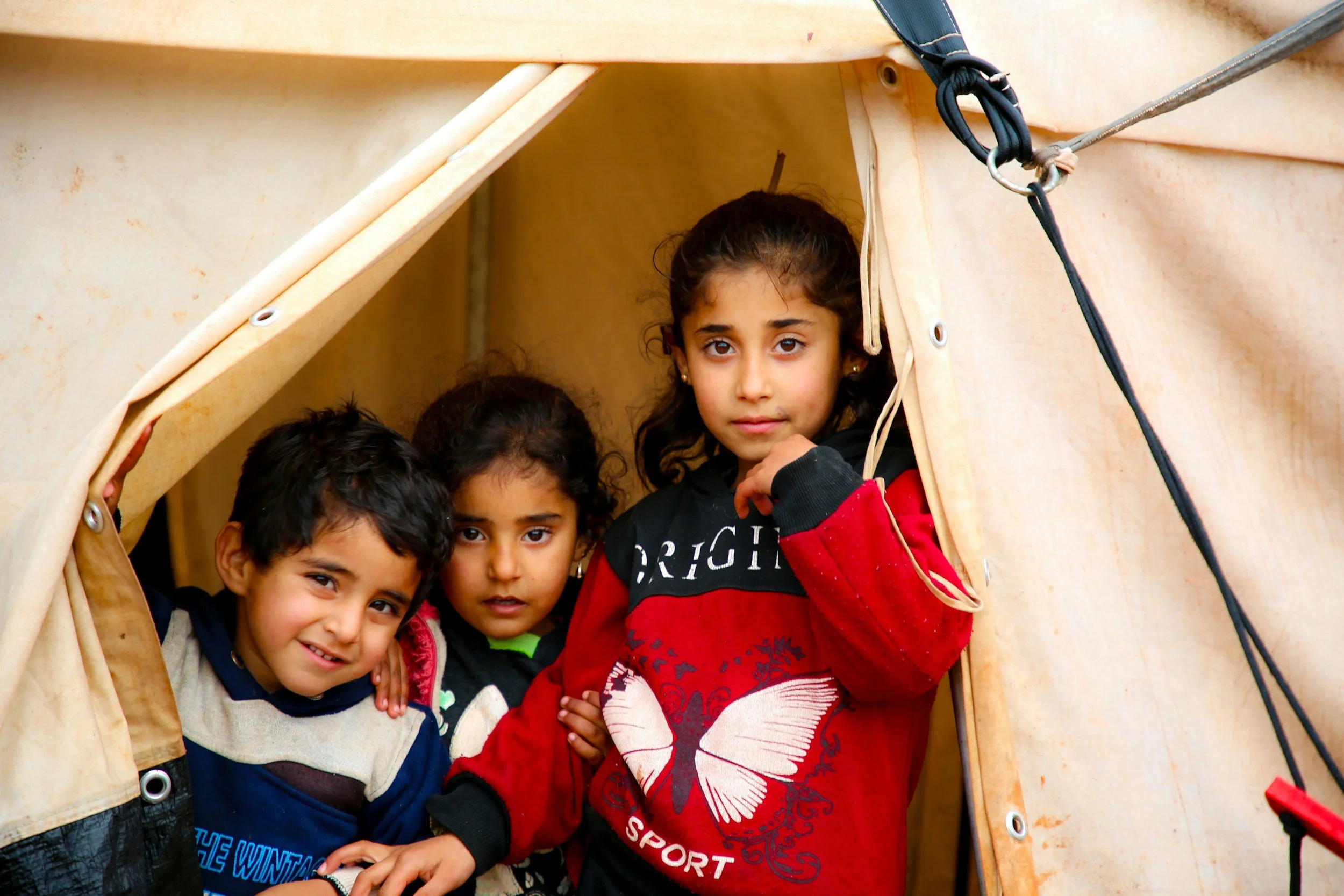 Three young children looking out from a tent opening.