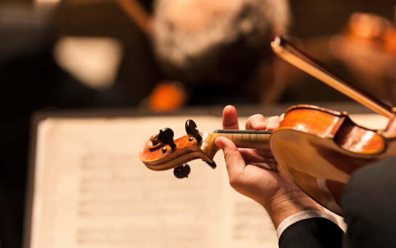 Close-up of a person playing a violin, with sheet music in the background.