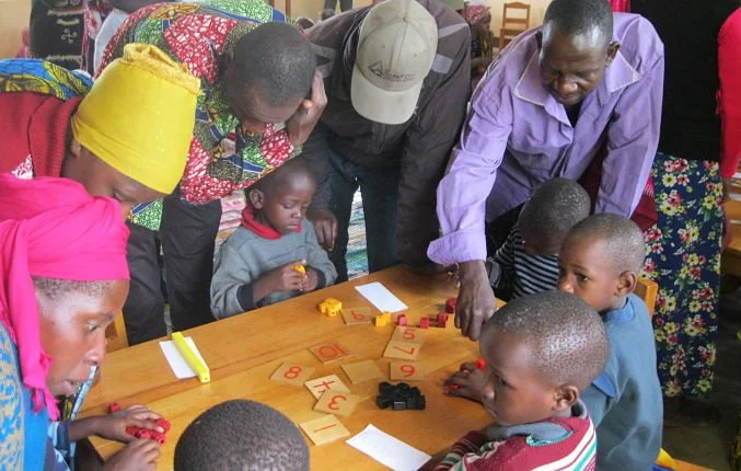 Group of children and adults gathered around a table playing a board game with numbered pieces.