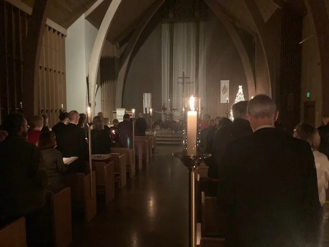 A congregation gathered in a church for a service, with candles and an altar at the front, during a nighttime or evening service.