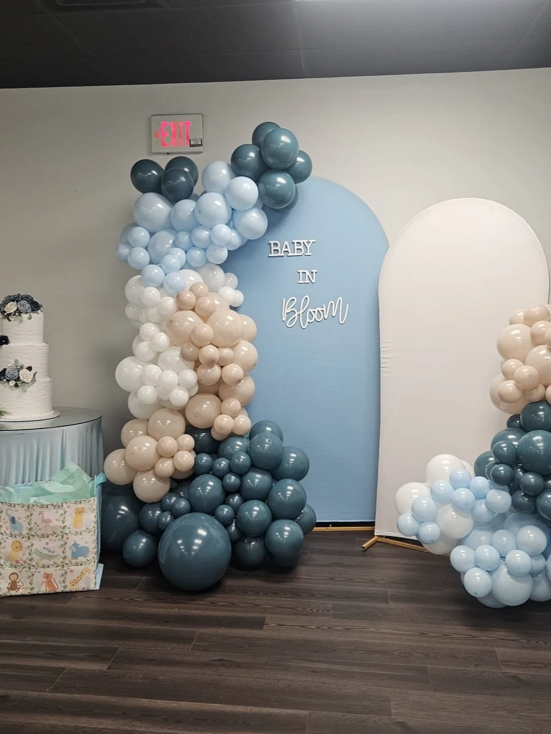 Decorative baby shower setup with pastel balloons, a cake, and a sign that reads 'Baby in Bloom'.