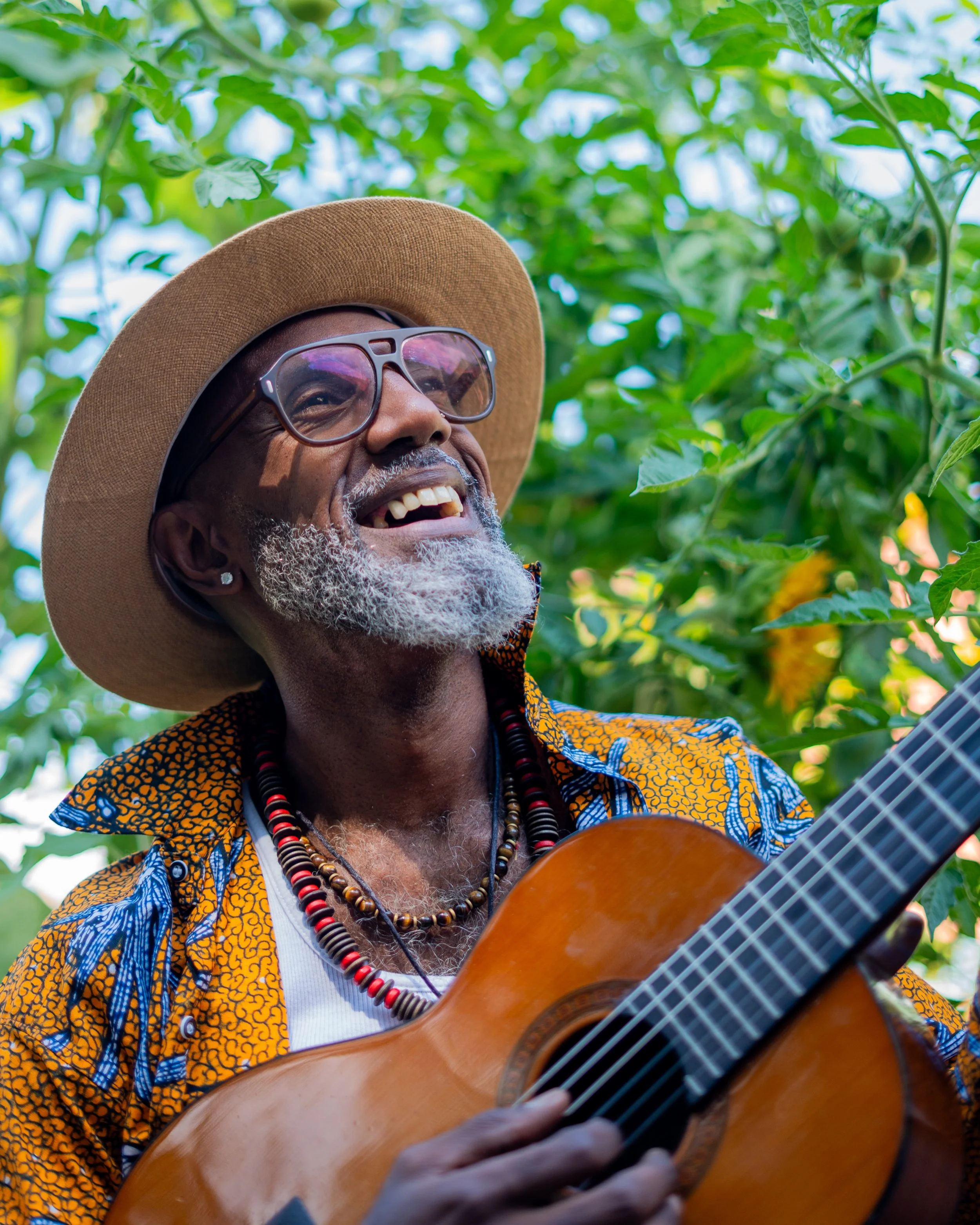 Close-up of a smiling middle-aged man with a beard and dreadlocked hair, wearing a black sweater against a plain background.