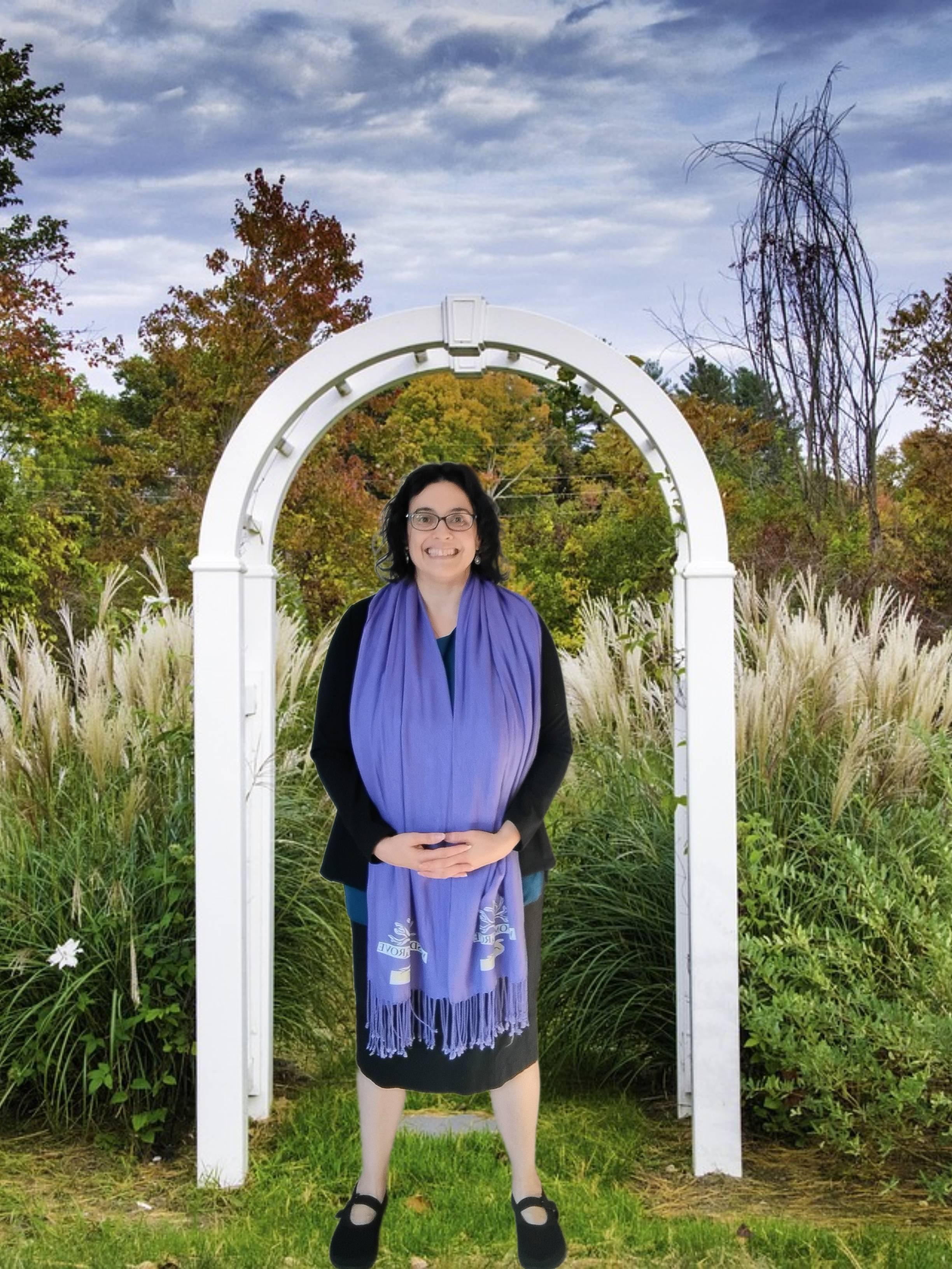 Downers Grove DuPage County inclusive wedding officiant Sarah Woodard from Wisdom Grove standing under a while arch with hands clasped in front wearing purple shawl