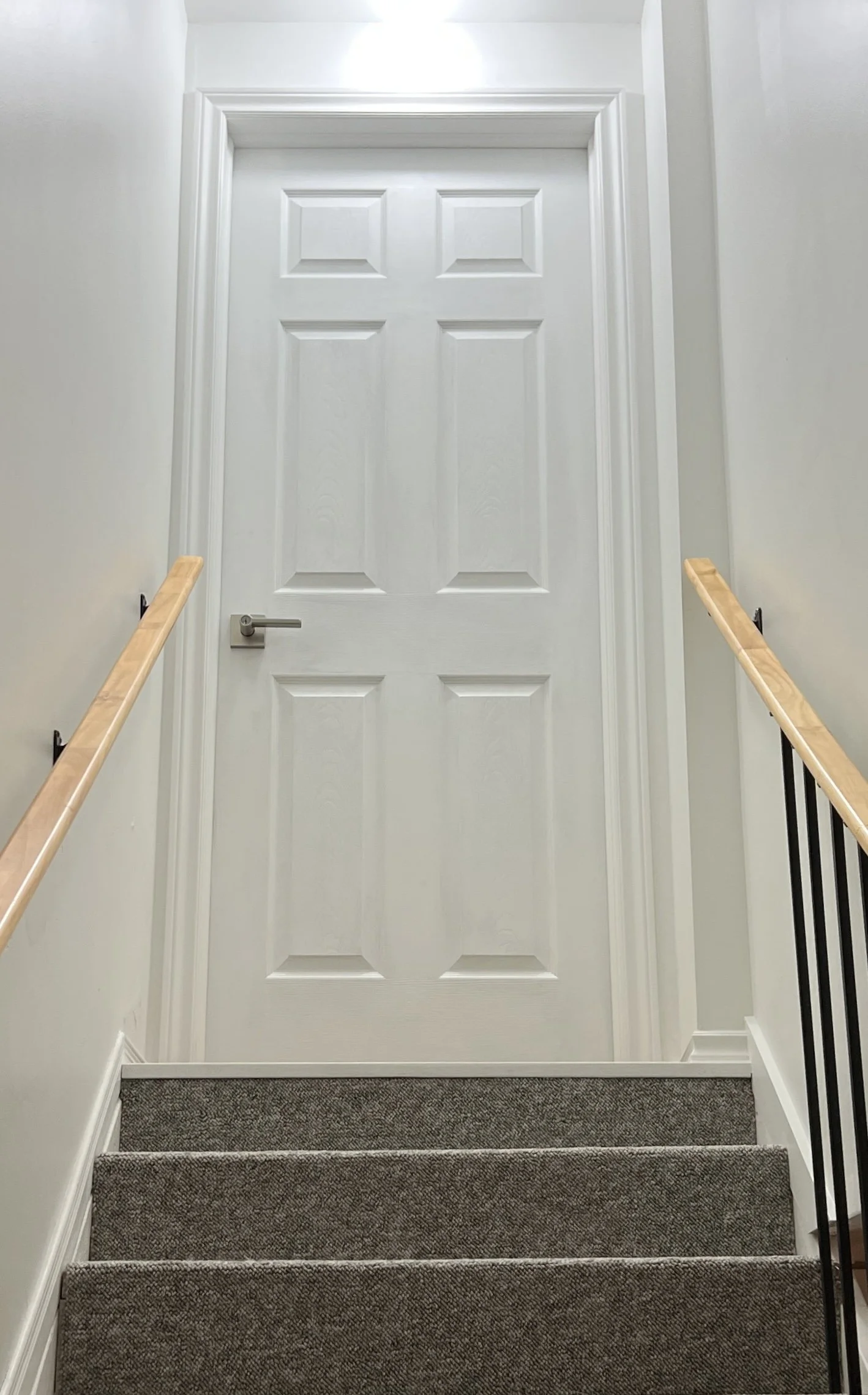 Indoor staircase leading to a closed white door with wooden handrails on both sides.