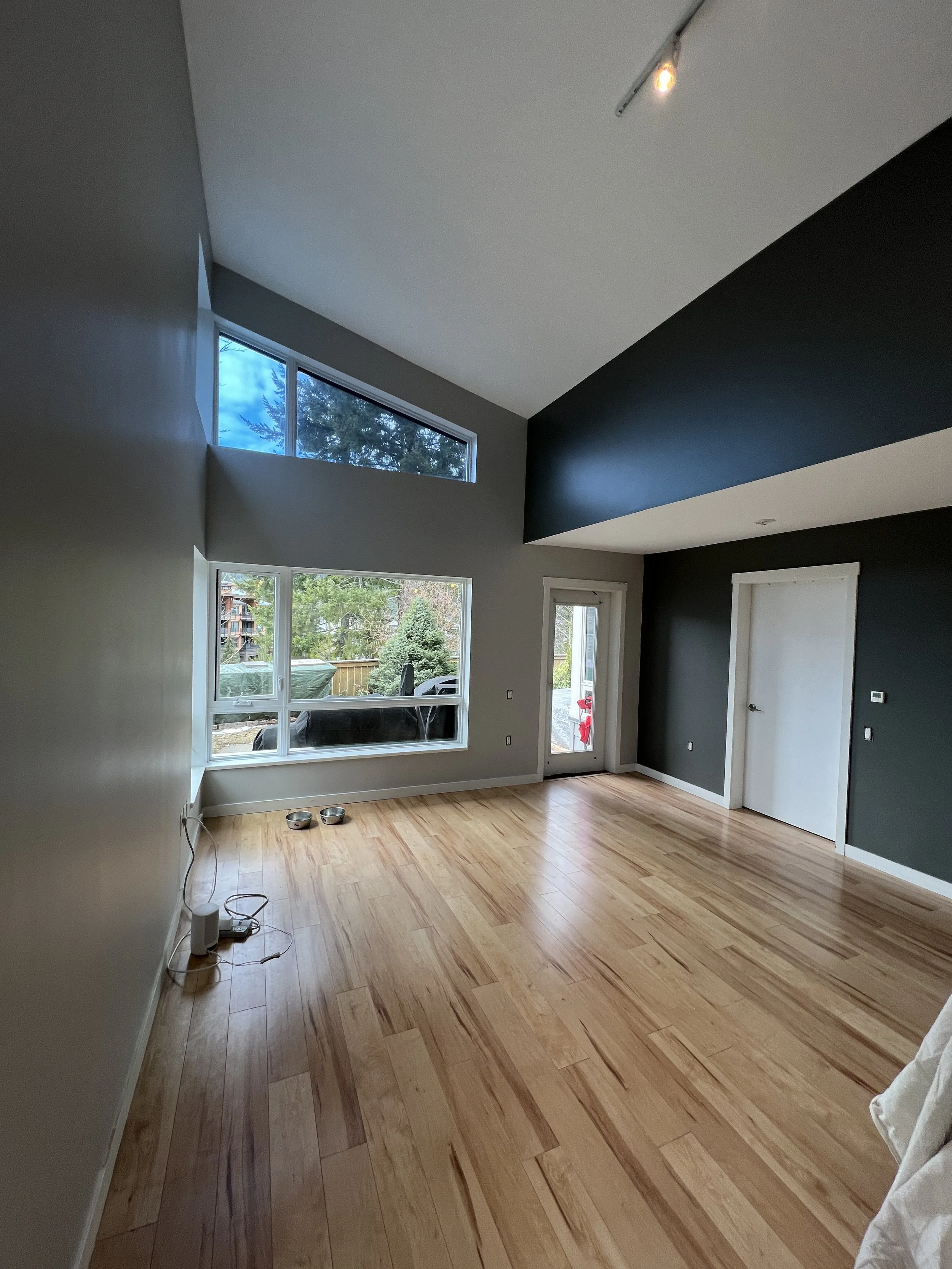 Empty room with hardwood floor, high ceiling, large windows, and dark accent wall.