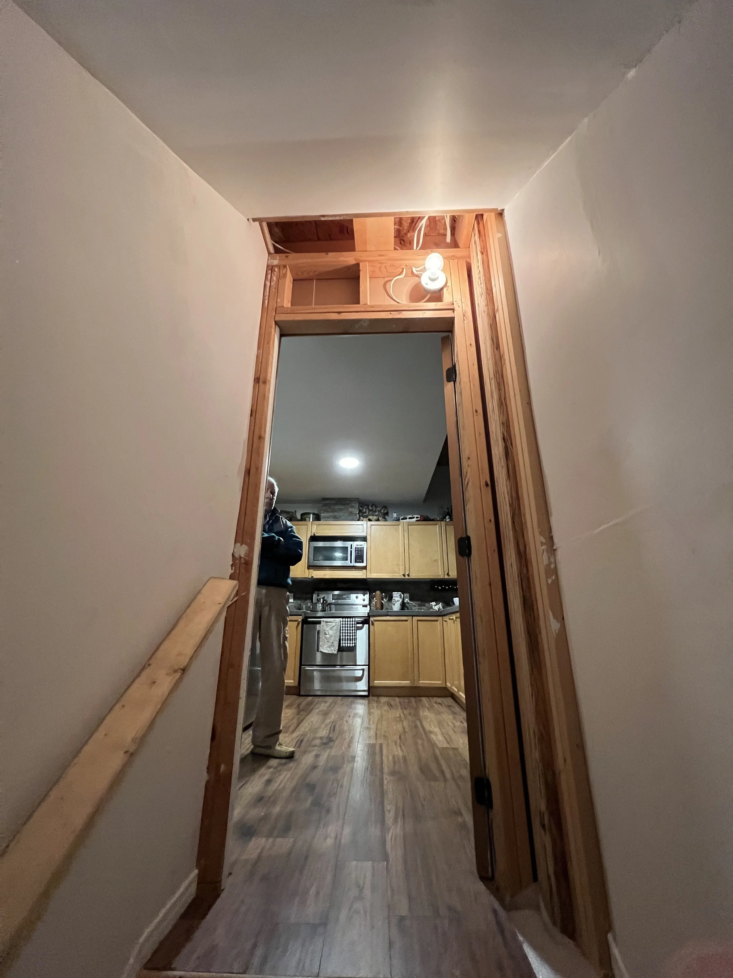 View from a staircase leading into a kitchen with wooden cabinets, stainless steel appliances, and a person standing near the counter.