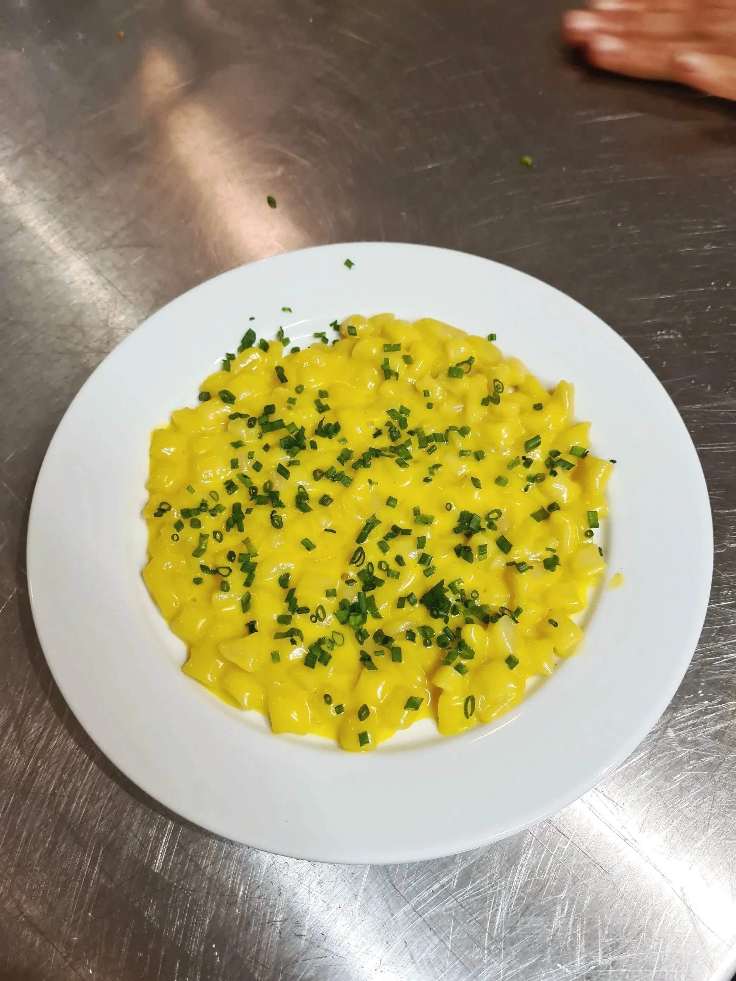 Creamy yellow pasta topped with chopped green herbs on a white plate.