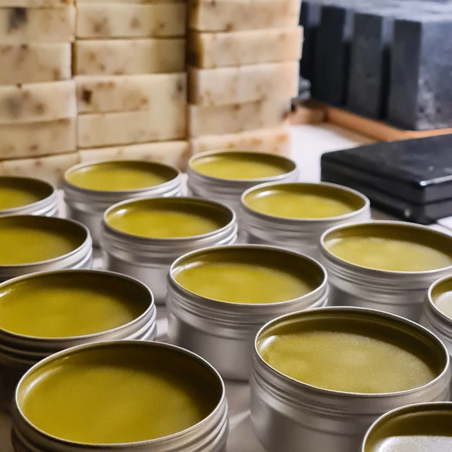 Multiple open tins of yellowish-green wax or polish on a surface, with stacked wooden blocks in the background.
