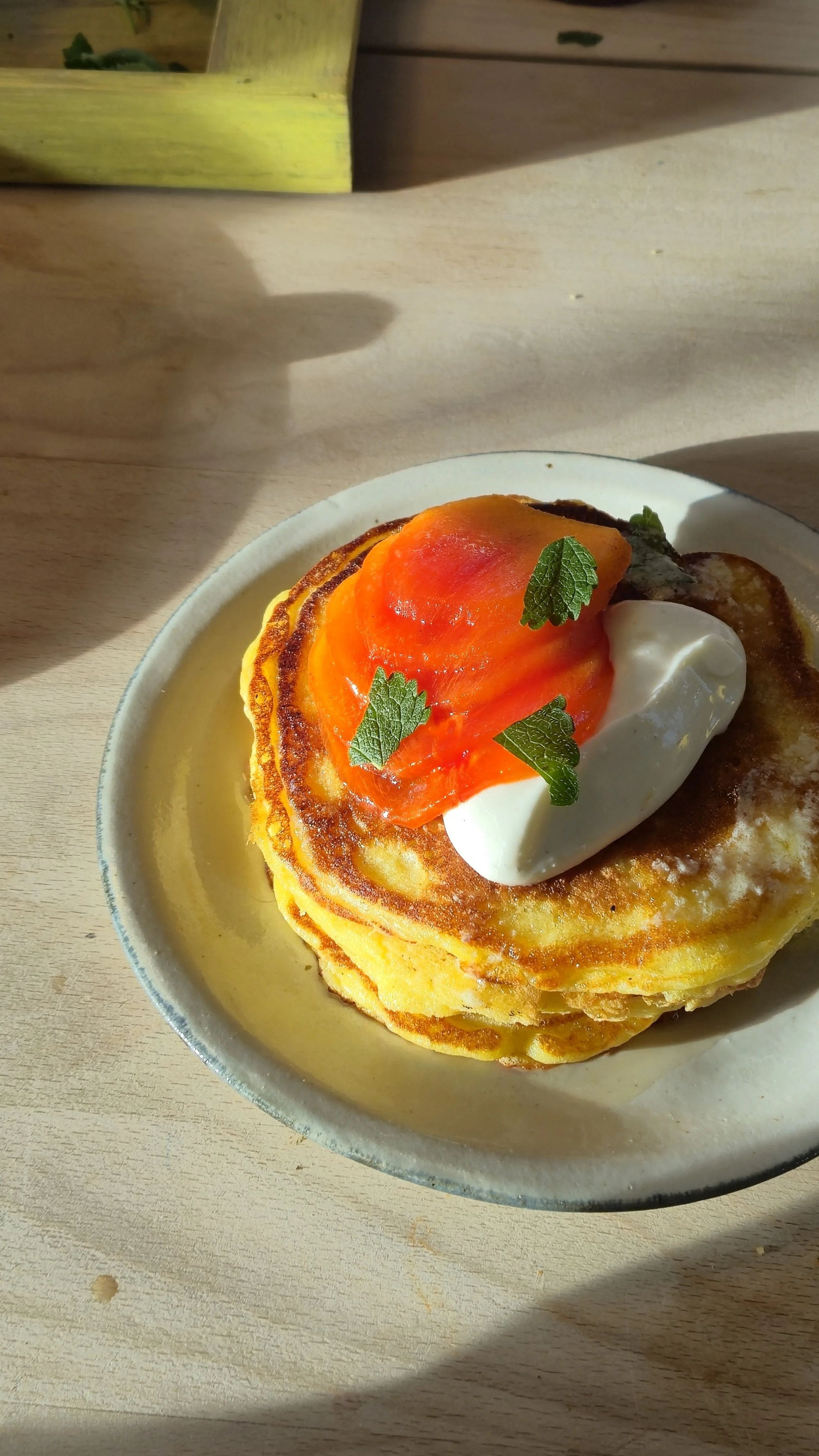 Stack of pancakes topped with a dollop of whipped cream, a slice of tomato, and garnished with small green leaves.