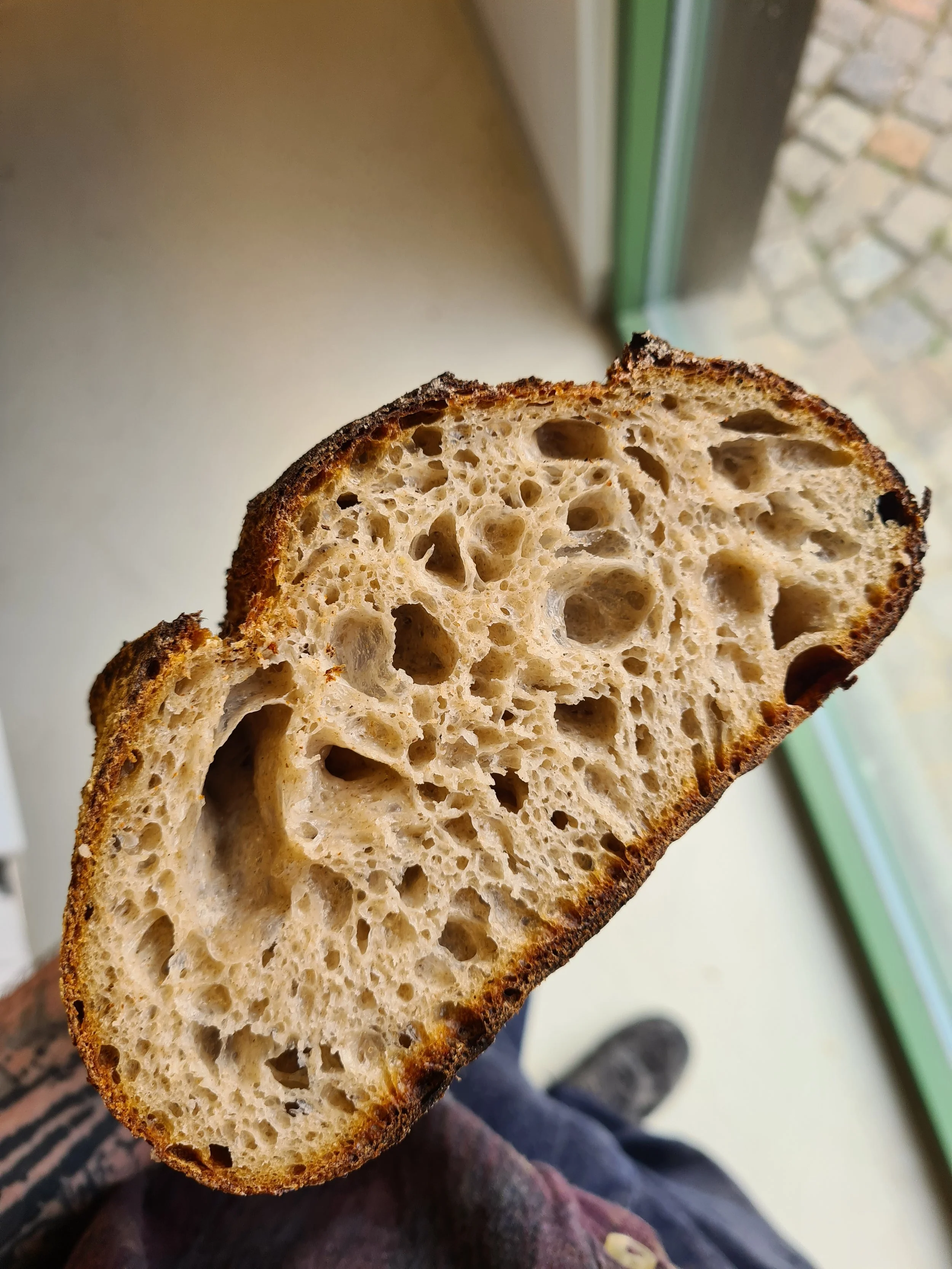 Close-up of a slice of sourdough bread showing an airy, hole-filled interior and a dark, crispy crust.
