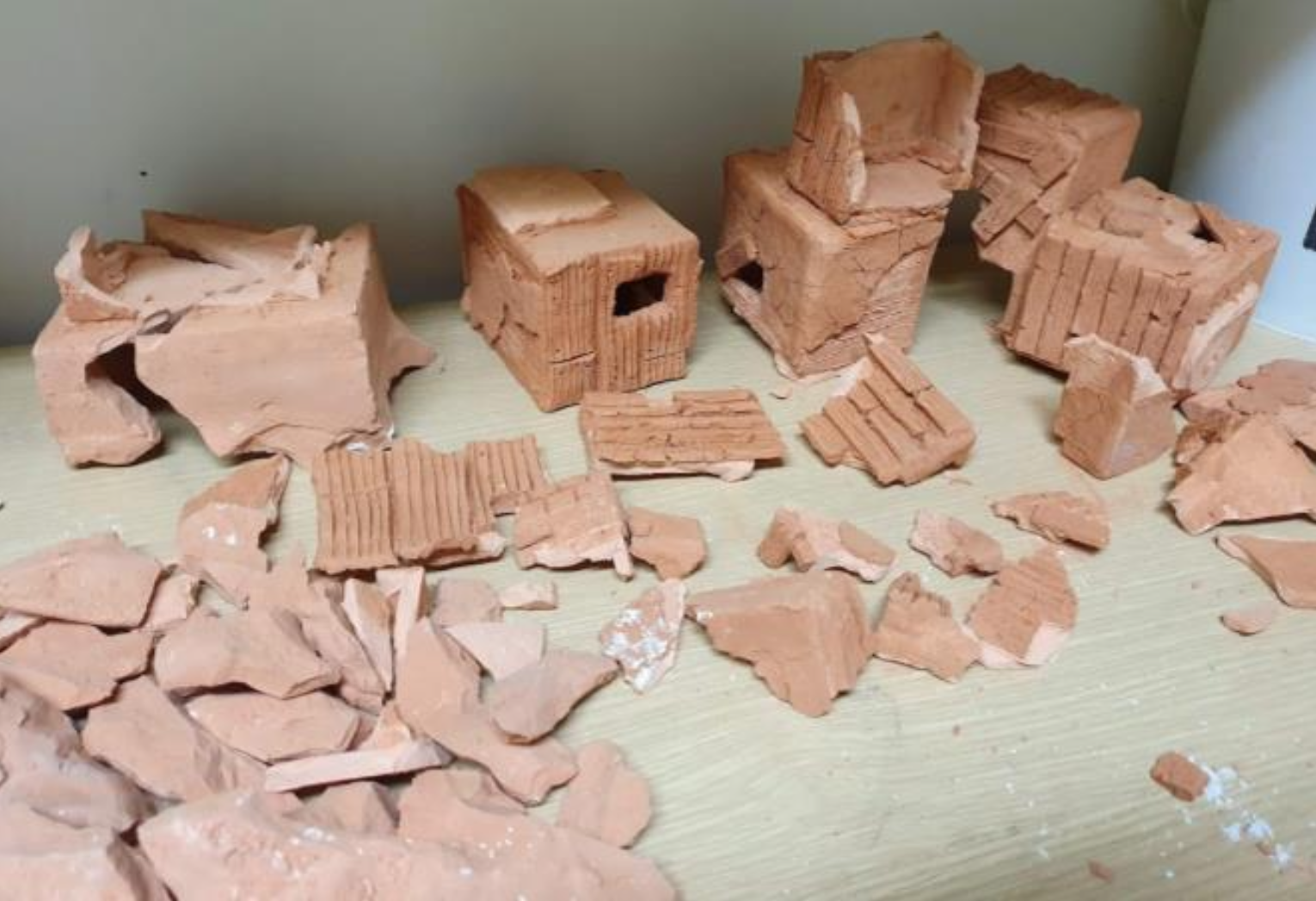 Broken pieces of red clay bricks and small brick structures on a wooden surface, some bricks have holes and ridges.