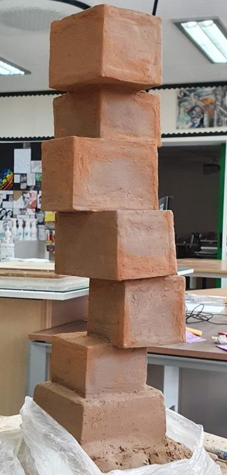 A tall stack of six red bricks placed on a plastic bag on a worktable in a classroom or workshop.