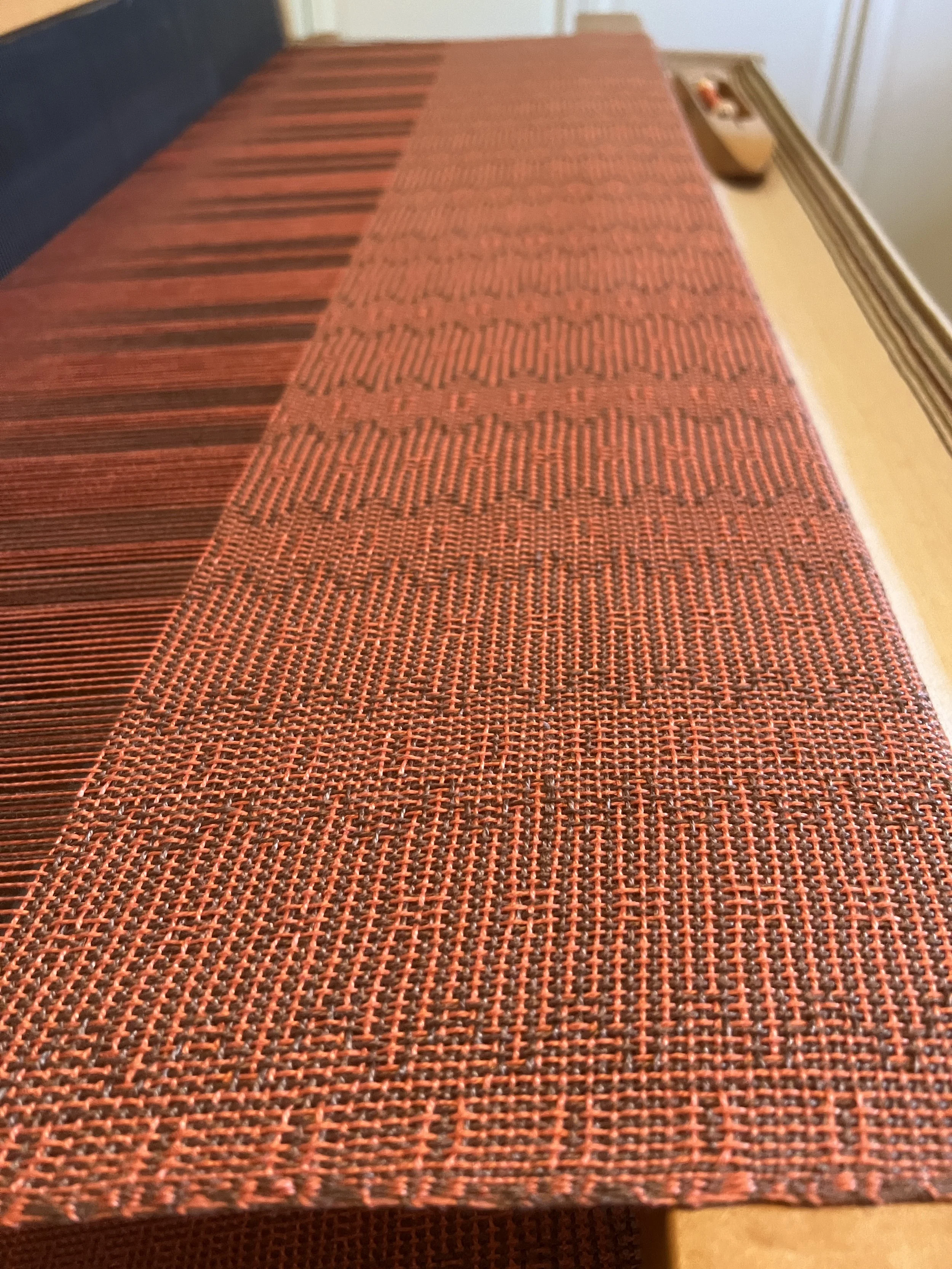 Close-up of an orange textured blanket on a wooden loom.