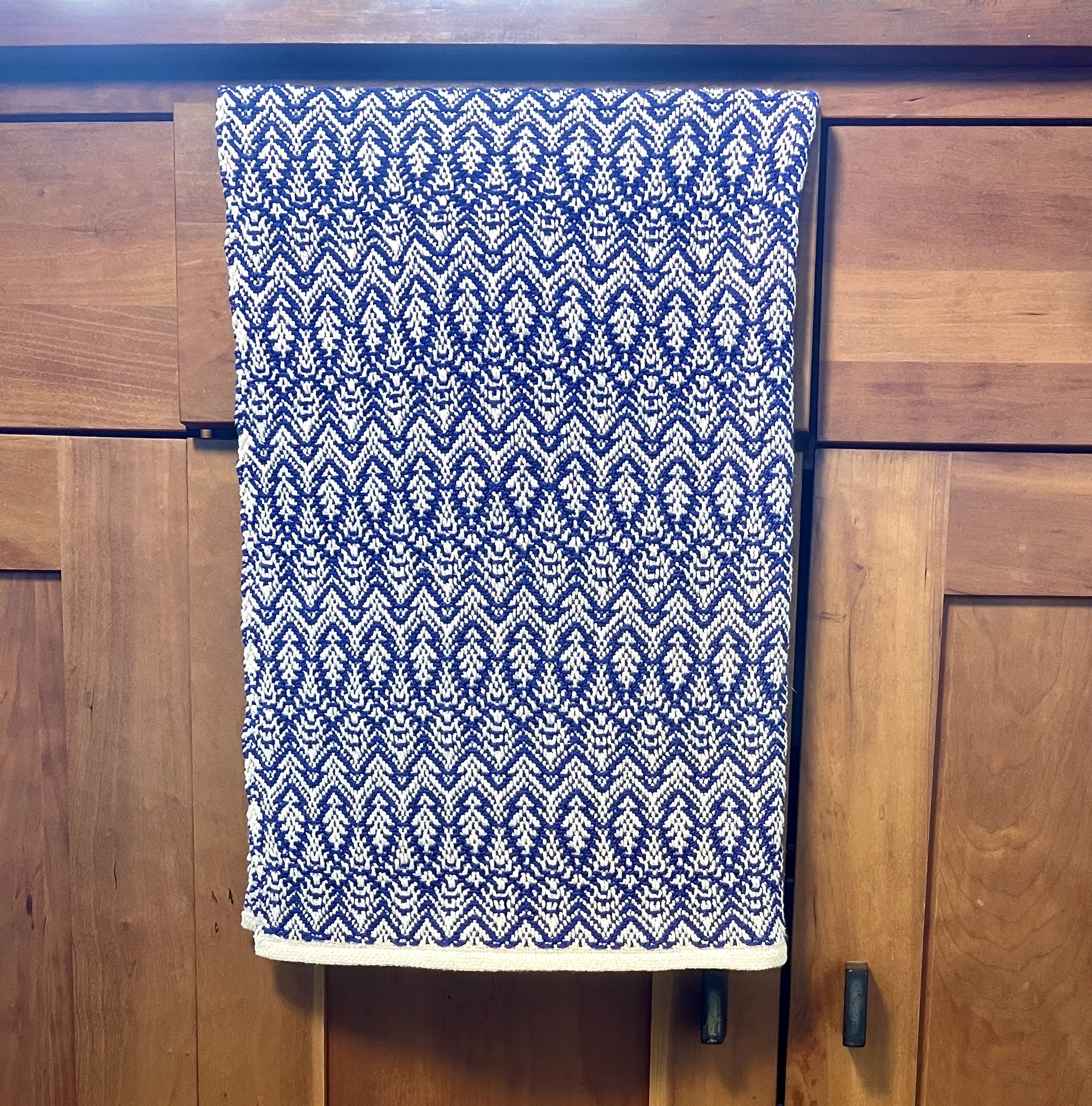 A blue and white patterned towel hanging on a wooden cabinet.