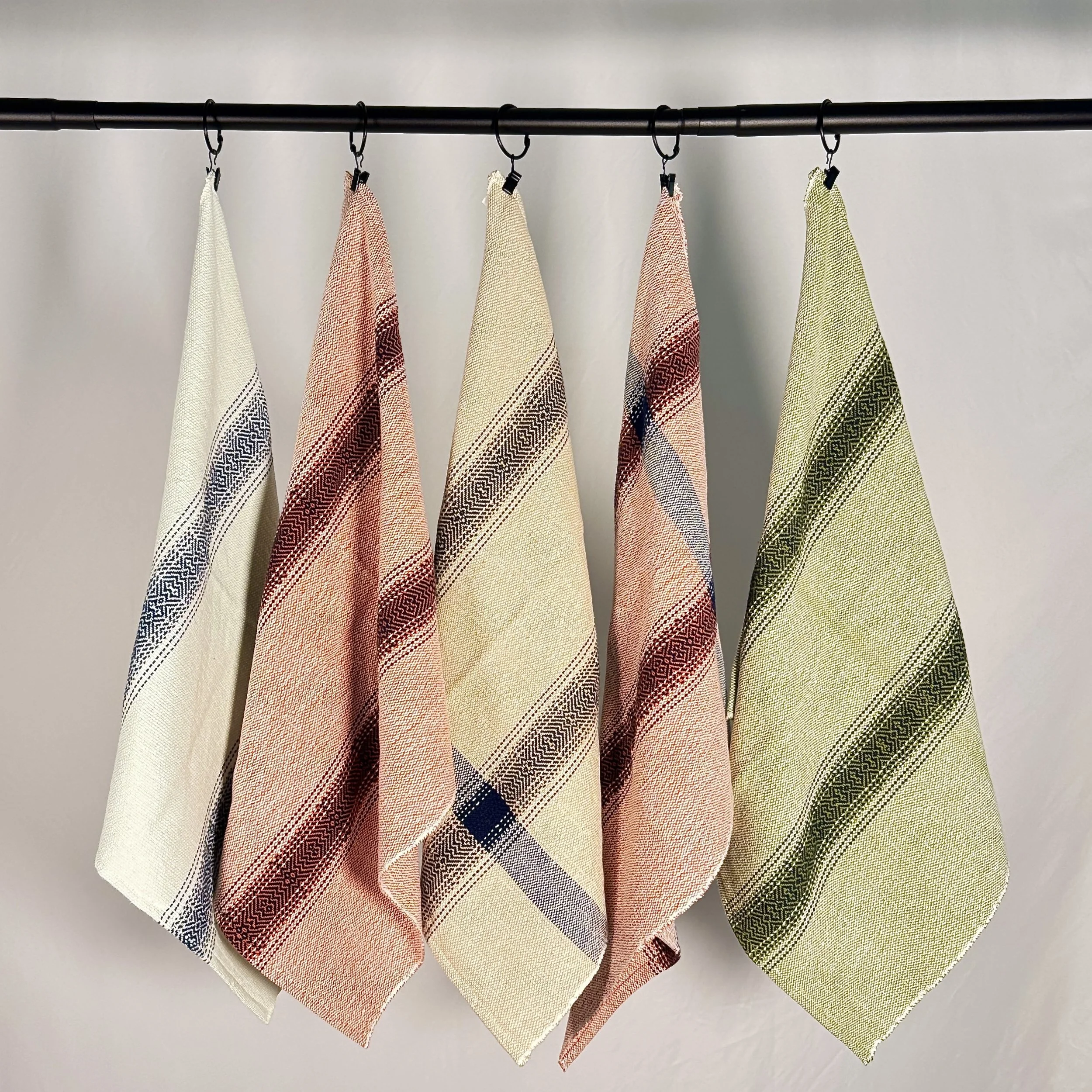 Five folded patterned towels hanging on hooks from a black rod against a white wall.