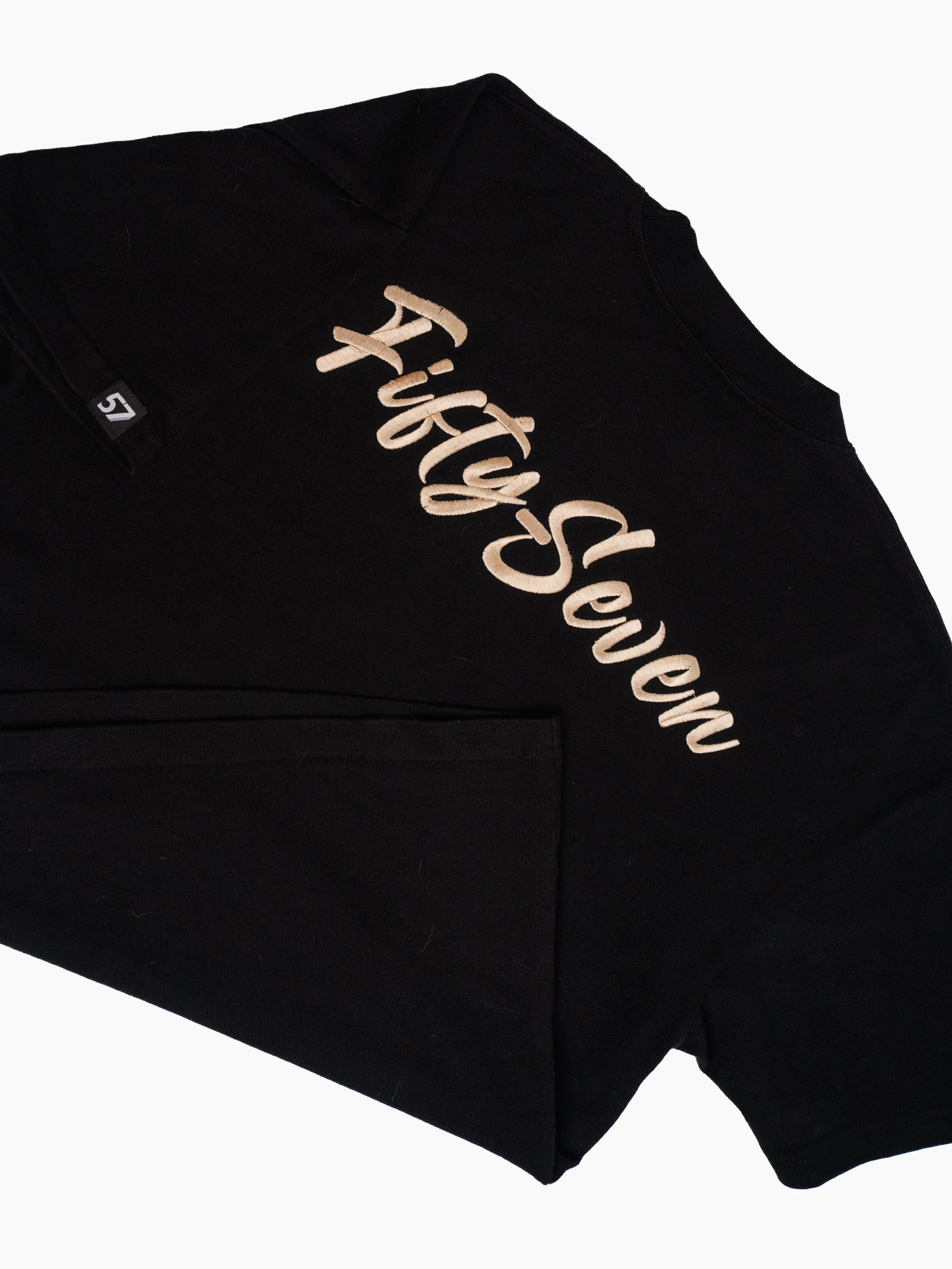 Close-up of a black sweatshirt with embroidered beige text reading 'Fifty-Seven' on the chest area. The image is cropped, showing only part of the shirt and focusing on the embroidered slogan.
