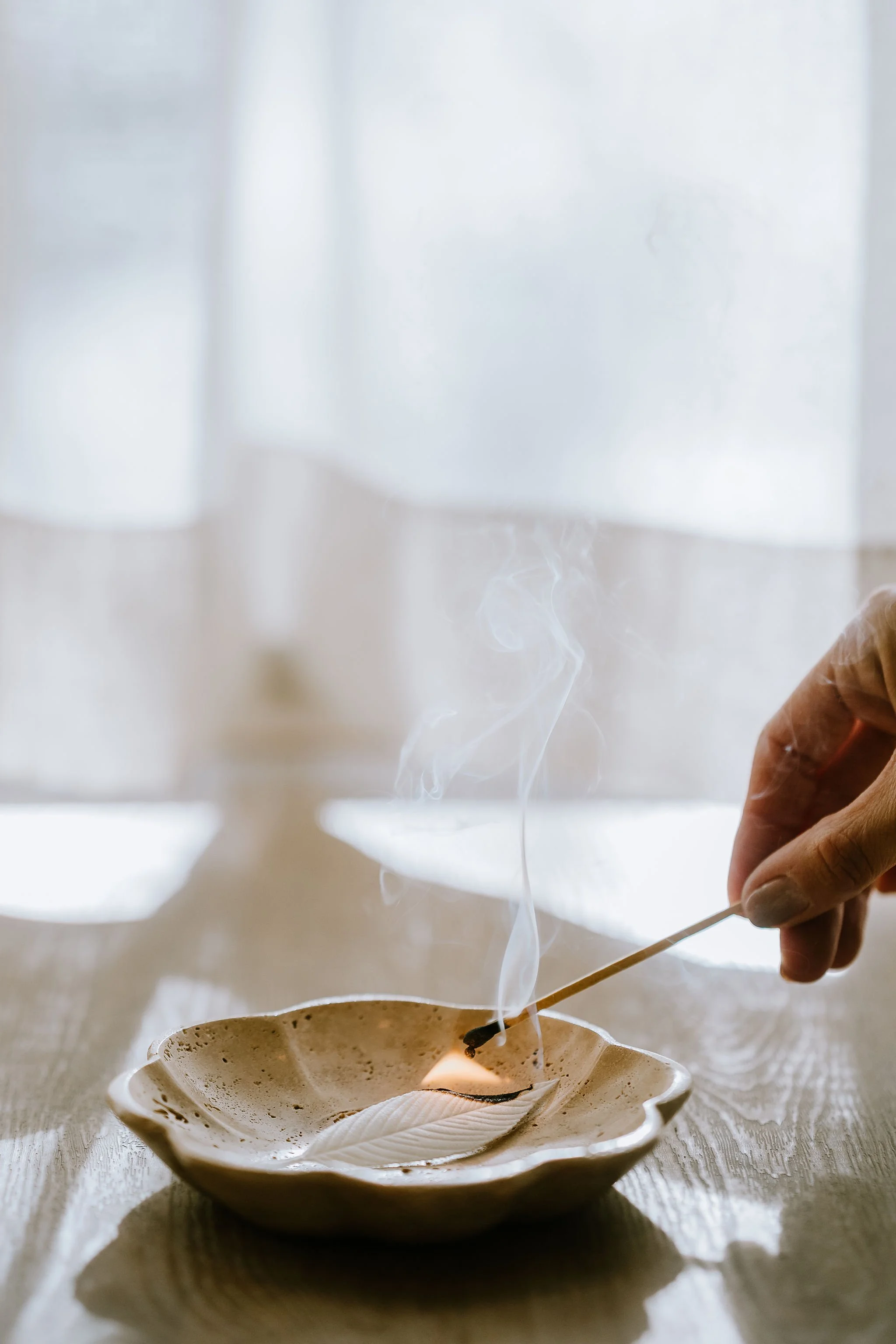Person lighting a traditional ceremony in a shell-shaped dish with a matchstick, with smoke rising from the lit substance.