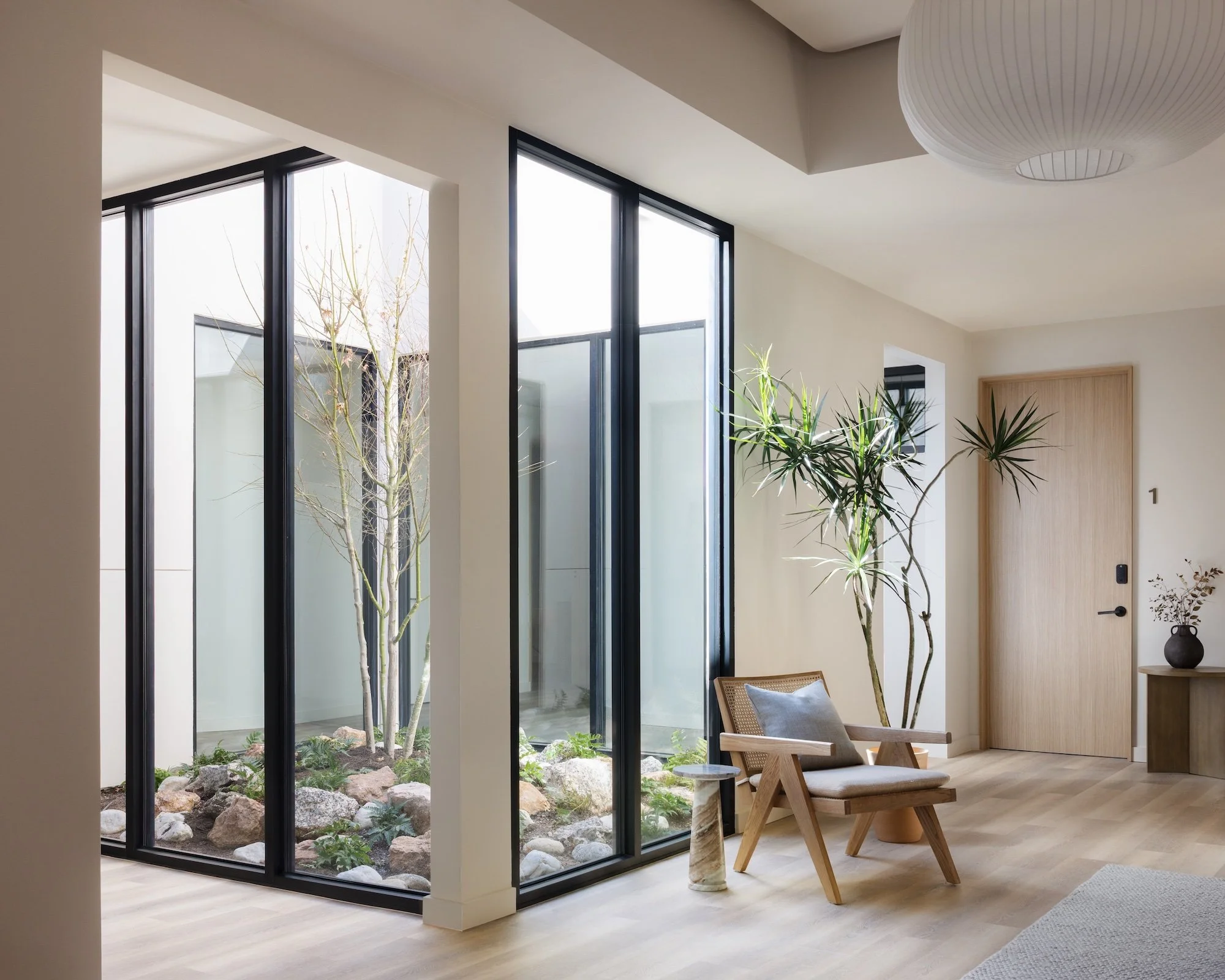 plant filled atrium surrounded by windows and chair and table in foreground