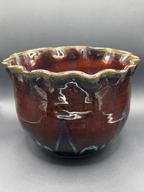 Handmade ceramic bowl with a dark brown glaze and a cloudy, uneven rim, displayed against a gray background.