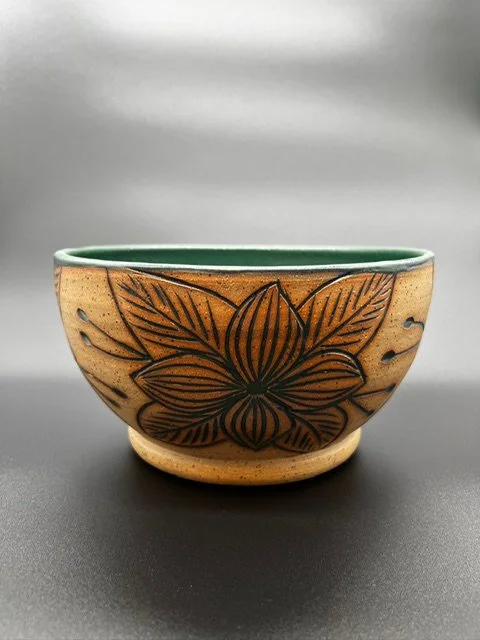 A ceramic bowl with a floral design on the outside and a green interior, set against a plain gray background.