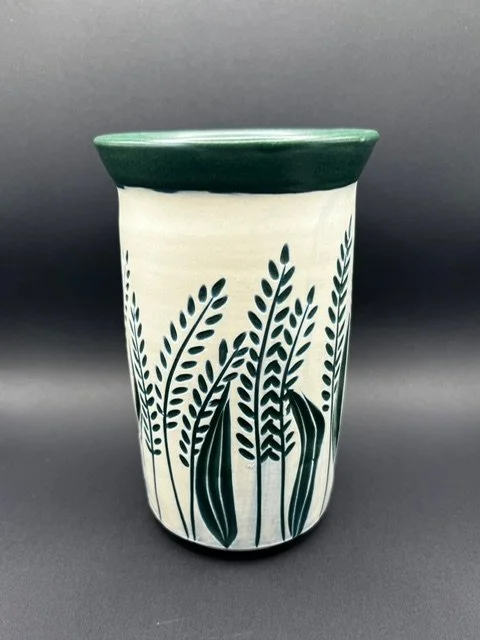 Ceramic vase with green rim and a white body decorated with dark green leaf and grass patterns.