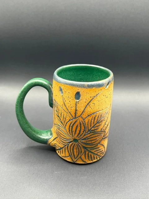 Colorful ceramic mug with a yellow body and green handle and interior, decorated with floral and dotted patterns.