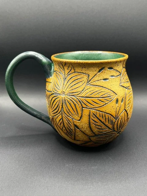Yellow ceramic mug with engraved floral patterns and a green handle and interior.