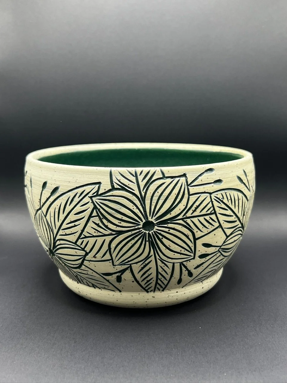Ceramic bowl with floral black line art pattern on a cream background, with a green interior, displayed on a gray surface.