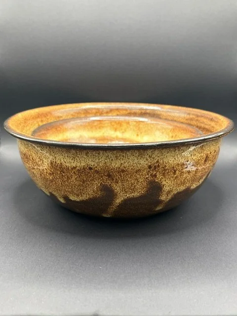 A ceramic bowl with a brown and yellow glaze, sitting on a black surface.