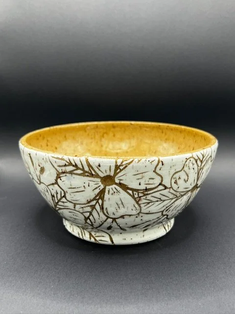 A ceramic bowl with a white exterior decorated with gold floral patterns and a gold interior, placed on a dark surface.