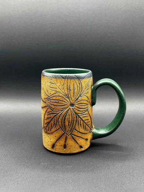 Ceramic mug with a floral design, yellow and green colors, and a green handle, placed on a dark background.