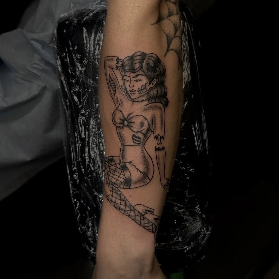 Tattoo of a stylized woman with short hair, fishnet stockings, and a revealing outfit, sitting with her arm raised behind her head.