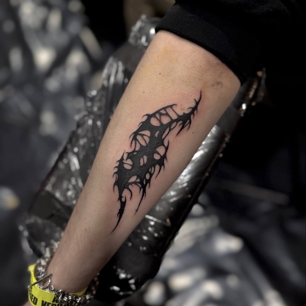 Black tribal-style tattoo on forearm, featuring jagged, flame-like shapes, in a tattoo studio.