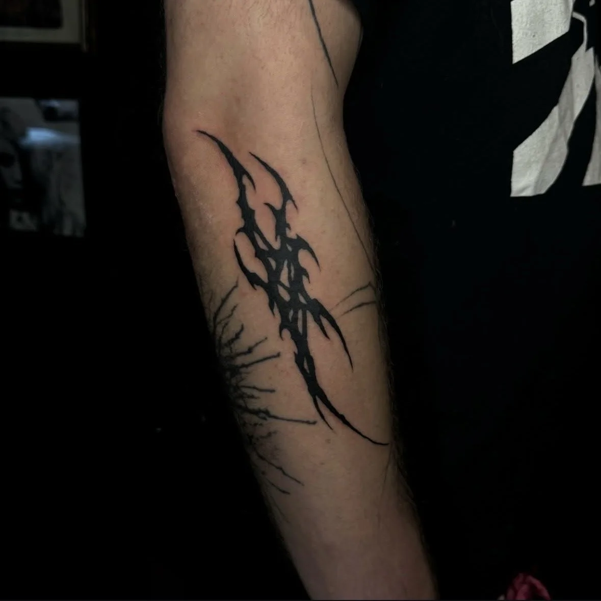Black tribal-style tattoo with sharp, jagged lines on a person's forearm.