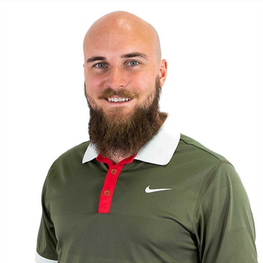 A man with a bald head and a full beard wearing a green Nike polo shirt with a white collar and red button placket, smiling at the camera