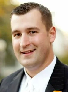 Close-up photo of a man in a suit smiling outdoors