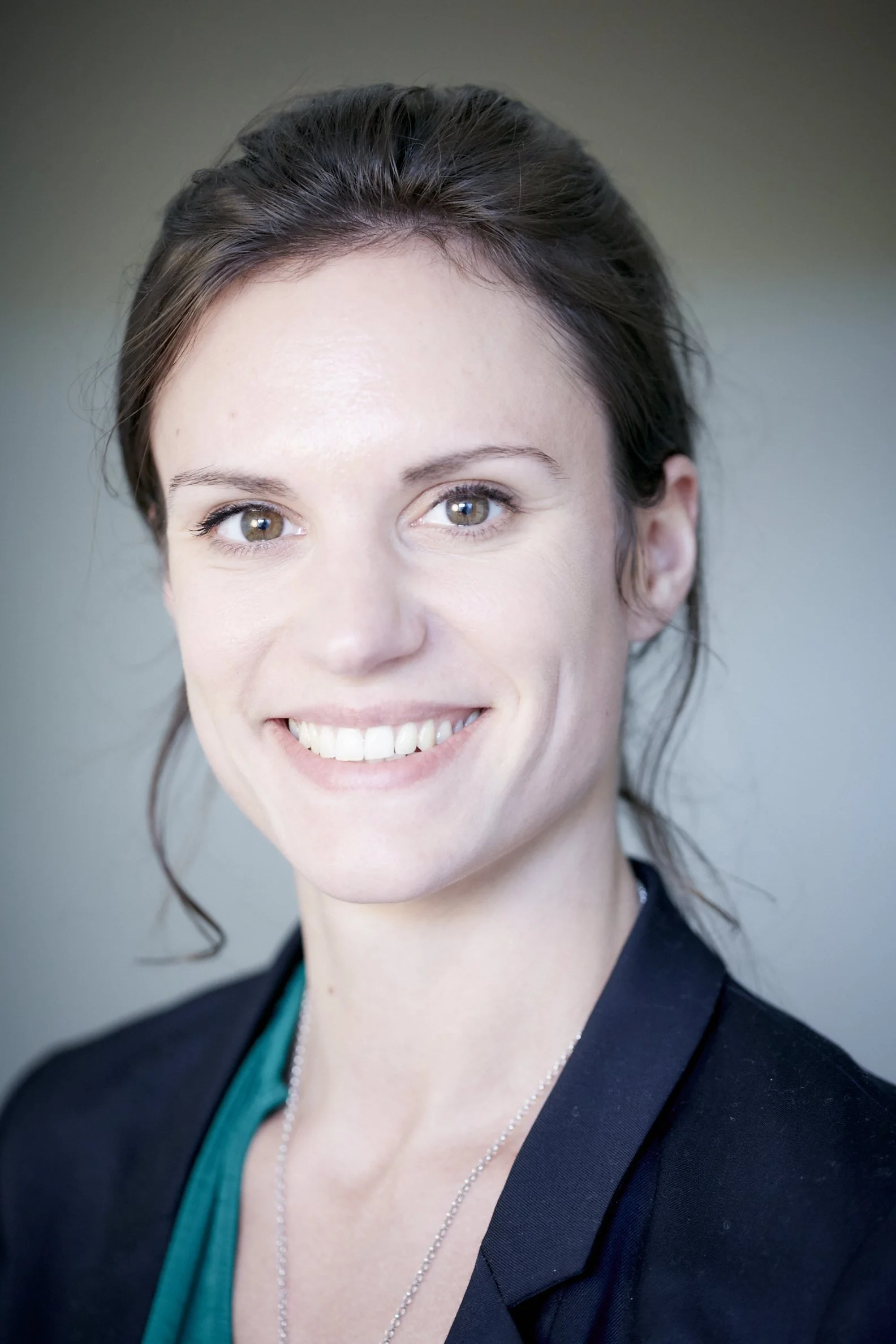 Close-up of a smiling woman with brown hair, wearing a black blazer and a teal top.