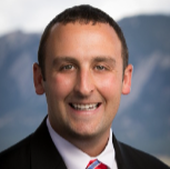 Portrait of a smiling man with short dark hair, wearing a suit and tie